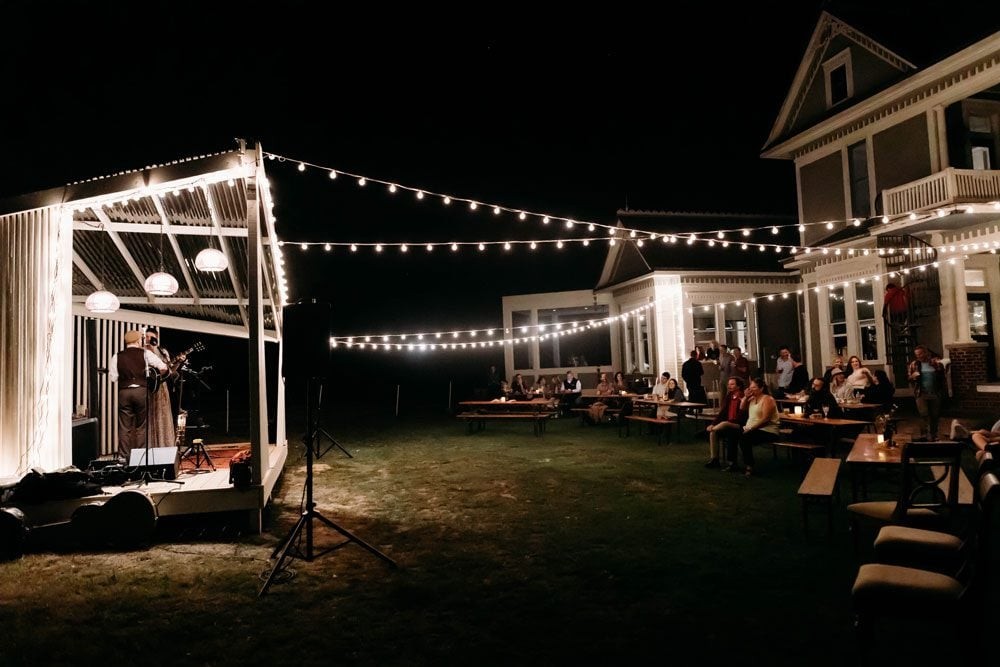 Night on the lawn at 10 CR 334 — string lights, music stage, and the 1903 house